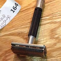 Close-up of vintage razor showing metal head and grooved black handle