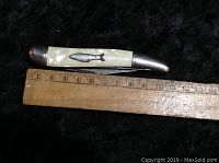 Closed view of vintage jackknife showing pearlized handle with metal fish design and ruler for size reference around 10 cm long when closed.