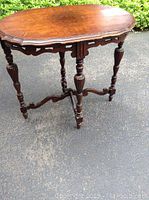 Full view of ornate wooden side table showing top, legs, and stretchers. Table has a scalloped edge and carved leg design.