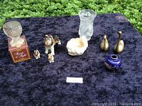 Full lot of Avon tealight holder with original box, cut glass vase 6", pair of heavy brass swans, oriental vase 3", ceramic Sheltie dog with 2 pups on chain, frog candle holder/soap dish on purple velvet background outdoors
