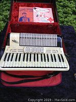 Ivory and black piano accordion with metal grille and two music books inside hard case with red velvet interior