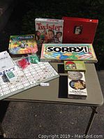 Seven board games arranged on a table showing packages and game pieces, including Scattergories, Twister, Sorry, Sequence, Waterworks, and Mille Bornes.