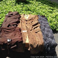 Photo of four clothing items laid out on a surface in sunlight including two long jackets and two dresses.