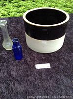 Three items arranged on dark cloth: blue apothecary bottle, ribbed bud vase, and brown/white crock.
