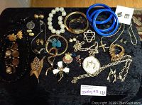 Full view of assorted jewelry laid on black cloth showing varied pieces including necklaces, earrings, bracelets, brooches, and pendants.