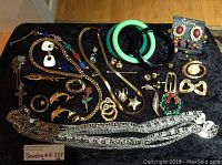 Overview of the entire jewelry lot displaying various necklaces, bracelets, earrings, and brooches arranged on a black fabric surface.