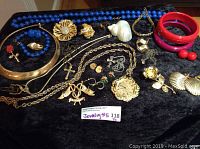 Full view of jewelry items displayed on black fabric including necklaces, bracelets, brooches, earrings, and items with gold tone and blue beads.