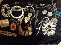Overview of assorted jewelry pieces including bracelets, necklaces, earrings, brooches on black fabric backdrop