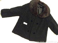 Full view of black Persian lamb fur coat with textured body and brown fur collar laid flat to show front side and sleeve length.