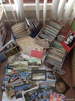 Overview of various postcards spread in and around two open boxes, showing both used and unused cards with varied international and US scenery.