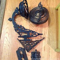 Top view photo of antique ornate metal wall sconce parts on wood floor showing sconce arm, canopy, decorative bracket and mounting pieces