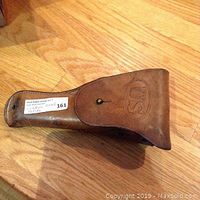 Front side of the leather holster showing the 'US' embossing on the flap and snap button closure with belt loop.