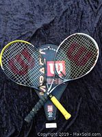 Photo of two Wilson tennis rackets and one Wilson branded cover on black fabric background.
