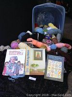 Photo of assorted yarn skeins spilling out of a blue storage bin alongside three craft books on knitting, stitching, and quilt making.