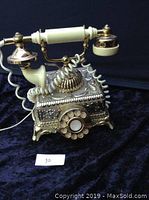 Front angled view of the ornate vintage French Victorian style rotary dial telephone with gold brass finish, showing detailed metalwork and rotary dial.