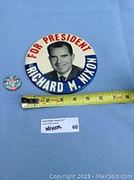 Top view of large Nixon For President button with ruler showing approximately 3.5 inch diameter, and smaller colorful Javits campaign button.