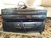 Two black VHS VCR players stacked with cables coiled on top, showing front panel details