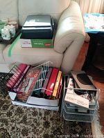 Multiple binders, wire paper basket, business card keeper, and iPad cover grouped in box and on floor in front of sofa