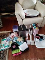 Photo of all items arranged near an armchair, showing placemats, garbage can, drawer dividers, dishes, trays, vacuum bags, and other small kitchen items.