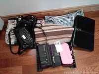 Photo showing assortment of purses and wallets arranged on the floor, featuring floral, striped, woven, and solid black bags
