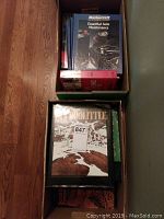 Photo showing two boxes of assorted books including a Mastercraft Essential Auto Maintenance book and a large hardcover bird and animal book.