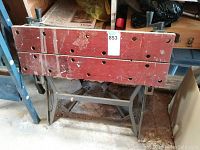 Workbench front showing wooden clamping surface with two rows of holes and fold-down legs frame.