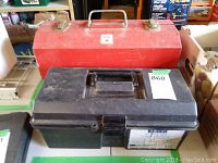 Two tool boxes placed side by side; one is a red metal Flaherty toolbox and the other a black plastic toolbox, both used condition.
