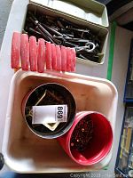 Plastic container filled with metal bolts, lag bolts, and red-handled torque keys on a white surface