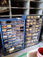 Front view of two large blue storage cabinets filled with small clear plastic drawers containing various hardware items such as screws, nuts, and bolts.