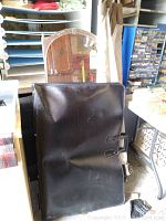 Black leather art portfolio case with buckle closures, visible scuff marks, upright position on floor.
