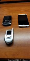 Photo showing three phones on a wooden surface: LG flip phone, Blackberry, HTC