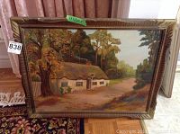 Framed oil painting showing a cottage in an autumn woodland setting, measured at 17.5 by 23.5 inches.
