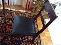 Side view of wooden dining chair showing black upholstered seat, carved backrest, and dark wood finish.
