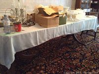 Fully extended dining room table covered with a white tablecloth, showing vintage style double pedestal base supports and general layout.
