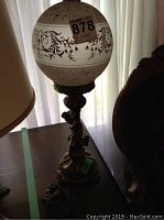 Full view of the metal cherub table lamp with decorated glass shade showing height and design.