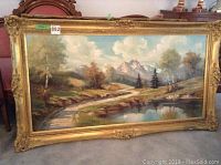 Framed oil painting depicting river scene with trees, mountains, and water.