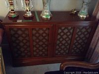 Front view of the cabinet showing lattice wood doors with fabric backing and some items placed on top for scale.