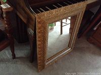 Full view of the hall mirror leaning against furniture showing rectangular shape with gold-painted carved wooden frame