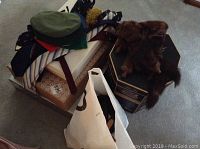 Assorted hats including a green beret, ties, scarves, and a brown fur hat on boxes and a bag on carpeted floor.