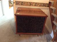 Front view of one wooden console speaker showing wood finish and fabric front panel with gold swirl design.