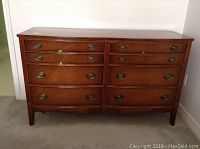 Front view of the dresser showing eight drawers with brass oval handles and polished wood finish.