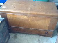 Front view of the wooden cedar chest showing the exterior with wear, scratches, and veneer delamination on top surface.