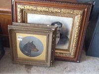 Three framed photo prints stacked against each other, two showing dogs and one showing a couple in ornate frames.