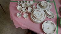 Tabletop display of multiple Royal Albert and Queens Moss Rose china items including stacks of plates, cups, and serving pieces all with floral and gold trim design.
