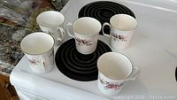 Five Royal Albert Lavender Rose mugs arranged on a kitchen stovetop, showing overall condition and design.