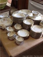 Full view of organized stacks of plates, teacups, and covered serving bowls placed on a table.