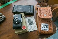 Vintage Kodak Pocket Camera, portrait attachment, instruction booklet, negative albums, and leather case displayed on a wood table.