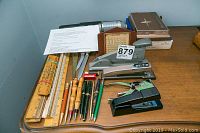 Full lot on wood desk showing rulers, pens, staplers, letter openers, calendar, list finder