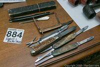 Photo showing several antique straight razors and folding pocket knives arranged on a wooden surface with typewritten label.