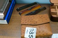 Photo displaying brown ostrich leather case with initials, a comb, and brush next to books on a shelf.